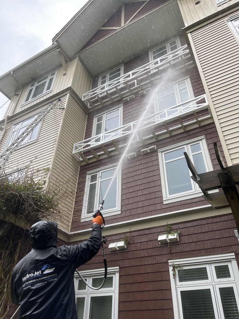 HydroJet crew member washing the upper exterior wall of a multi-family building